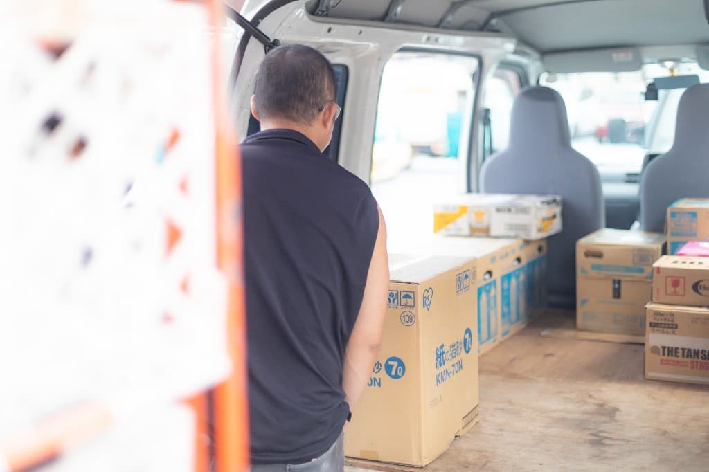 軽貨物車の荷室に荷物を積み込むドライバー